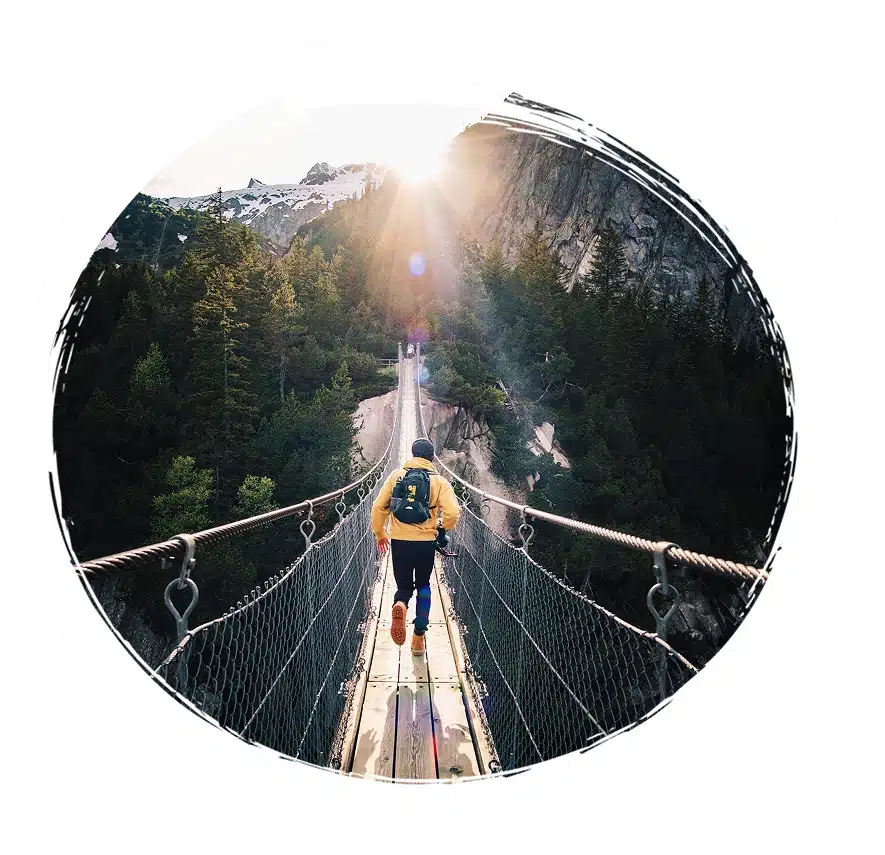 Person on mountain suspension bridge at sunrise.